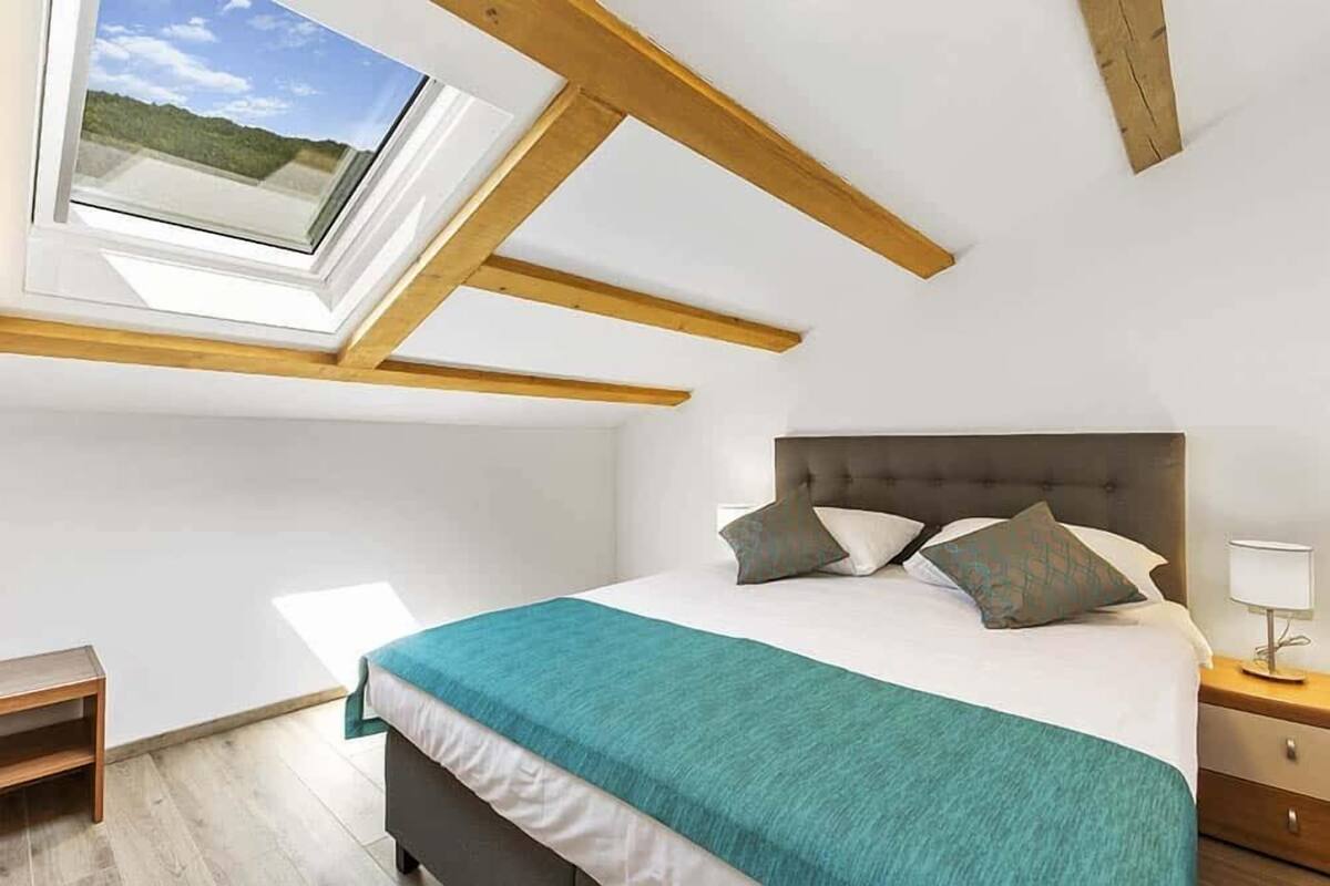 Ein Schlafzimmer mit Dachfenster, einem Bett mit Kissen, einem Nachttisch und einem Beistelltisch.