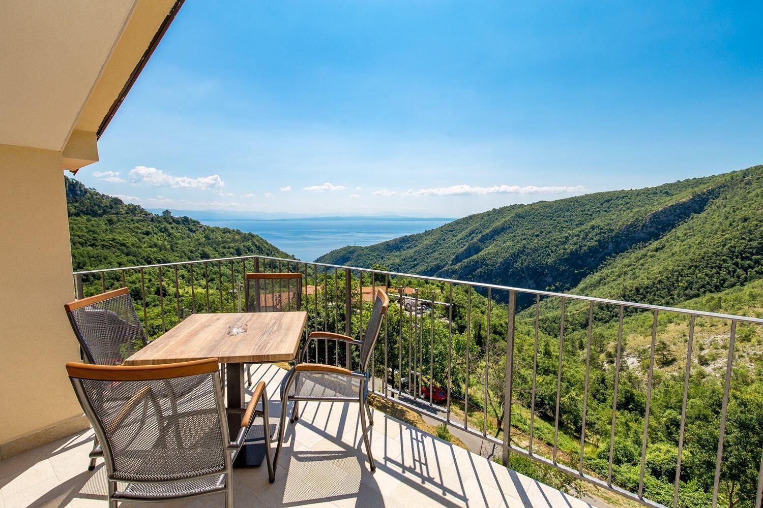 A balcony with a table and chairs overlooking a mountainous landscape and a body of water.