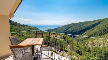 A balcony with a table and chairs overlooking a mountainous landscape and a body of water.
