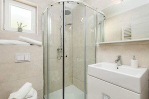 A modern bathroom with a glass shower enclosure, a white sink, and a mirror above it. - Pansion Villa Betina (Lovran)