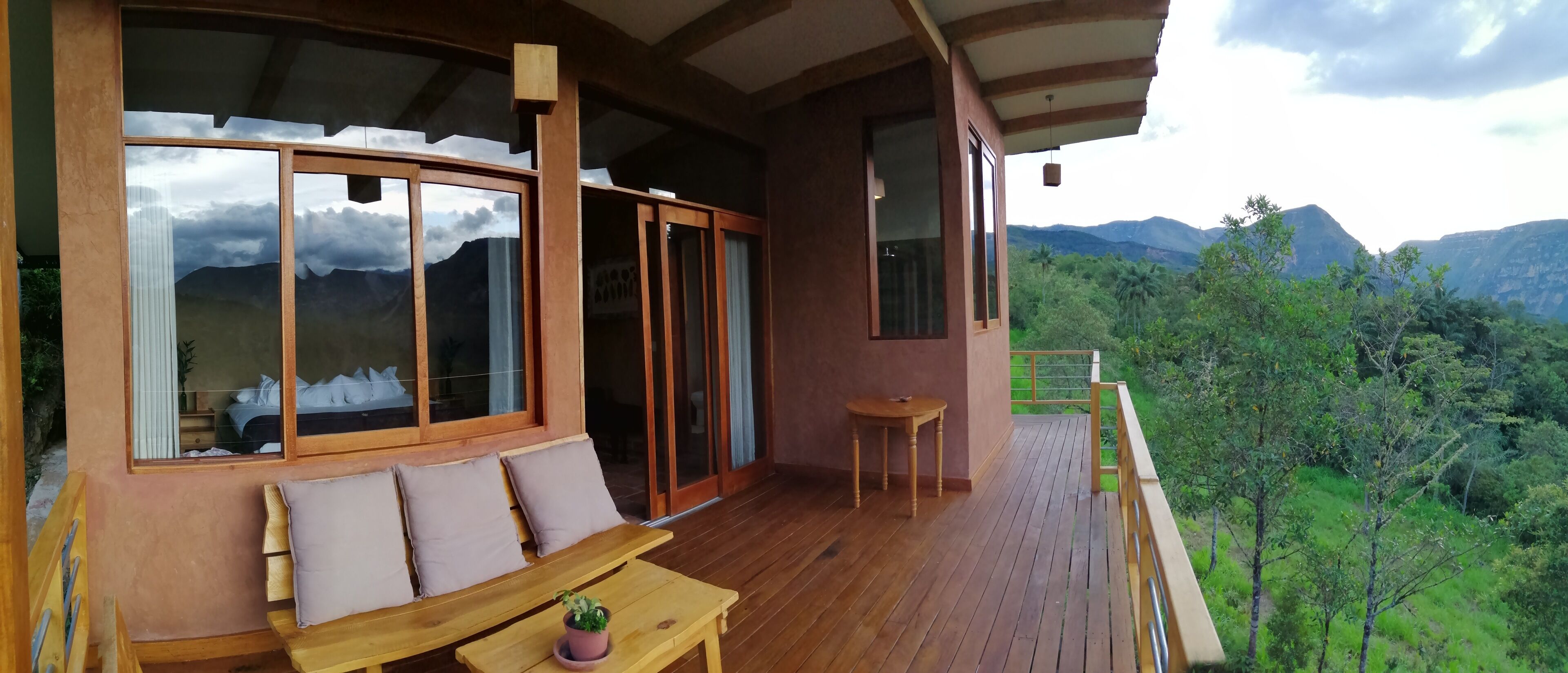 A wooden deck with a sofa and table, large windows with mountain views, and a balcony railing.