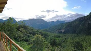 Una terraza de madera con una mesa, con vista a un valle exuberante y montañas al fondo.