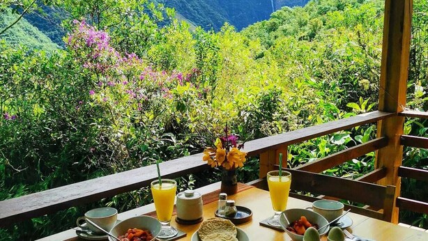 A dining table set with various dishes and drinks, overlooking a lush mountainous landscape.