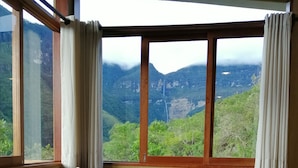 A room with a bed, a view of mountains, and a window with curtains.