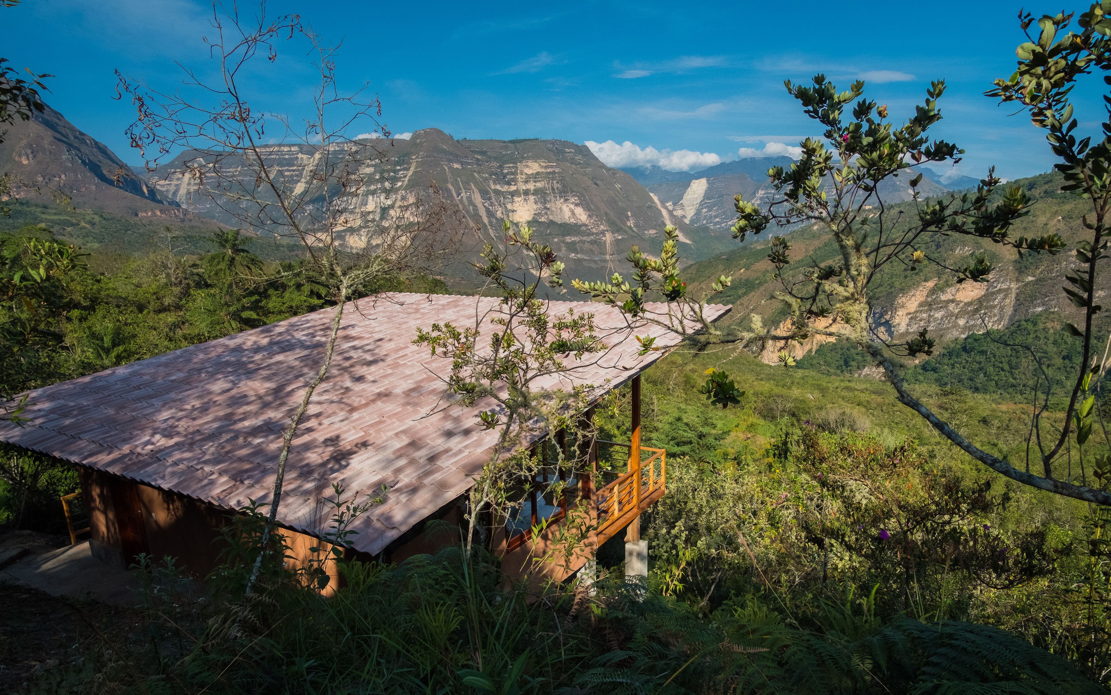 Une cabane en bois rustique, dotée d’un toit en pente, entourée d’une végétation luxuriante et avec des montagnes en arrière-plan.