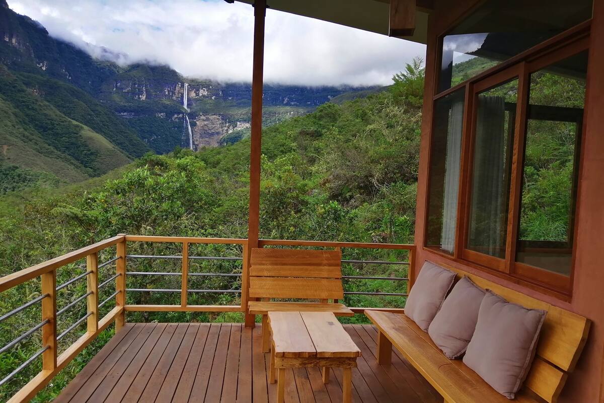 A wooden deck with a bench and table, overlooking a mountainous landscape with a waterfall.