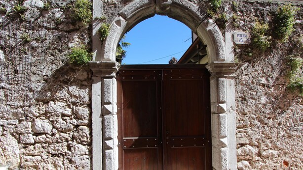 A stone archway with a wooden door, a sign reading "INTERN 25, 29", and a clear blue sky in the background. - Studio Isabel (Rovinj)