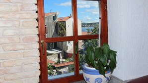 A window with a view of a coastal town, a potted plant, and a brick wall. - Studio Isabel (Rovinj)