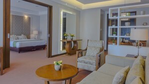 A hotel room with a bed, a chair, a sofa, a table with a vase, and a shelf with decorative items. - Mansion Garden Hotel (Olongapo)