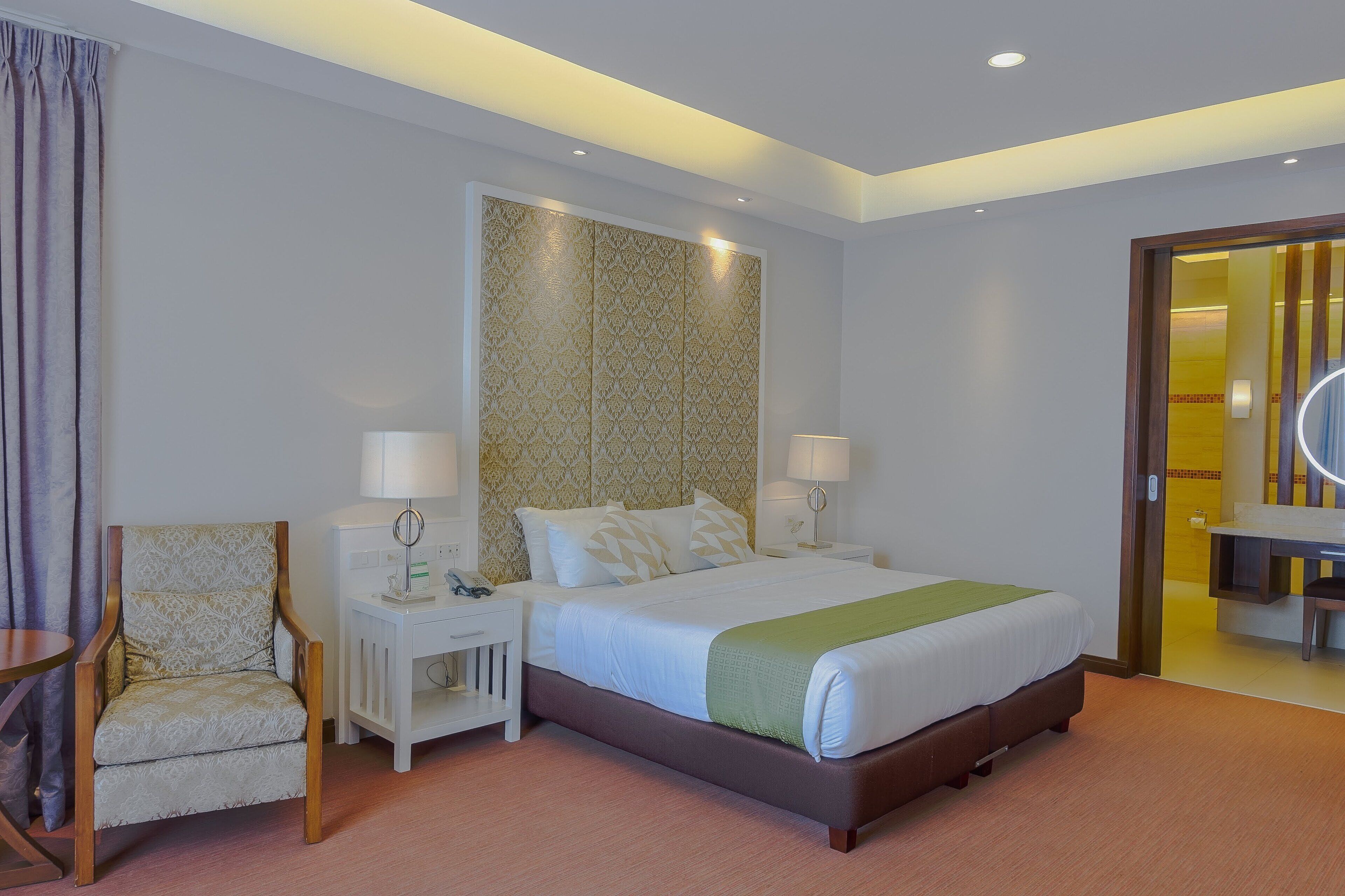 Habitación de hotel con una cama grande, dos mesitas de noche con lámparas, una silla y un armario.