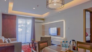 A modern hotel room with a sofa, dining table, chairs, a TV mounted on the wall, and a red rug. - Mansion Garden Hotel (Olongapo)