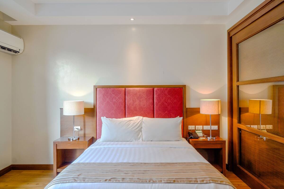 Een hotelkamer met een groot bed, twee nachtkastjes met lampen, een houten hoofdbord en een airconditioner aan de muur.