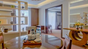 A modern hotel room with a round glass table, a wooden dining table, and a seating area with chairs. There are shelves with decorative items and a large window with curtains. - Mansion Garden Hotel (Olongapo)