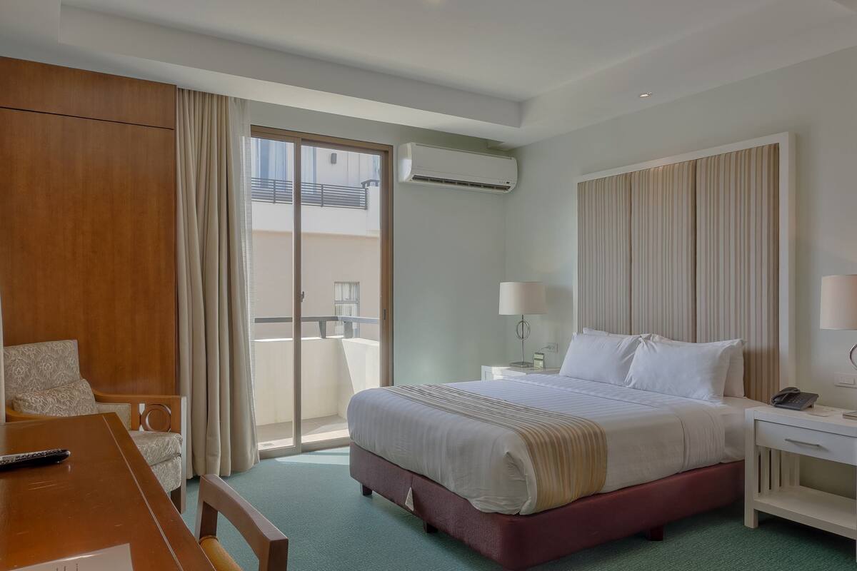 Een hotelkamer met een bed, een bureau, een stoel, een balkon en een airconditioning.