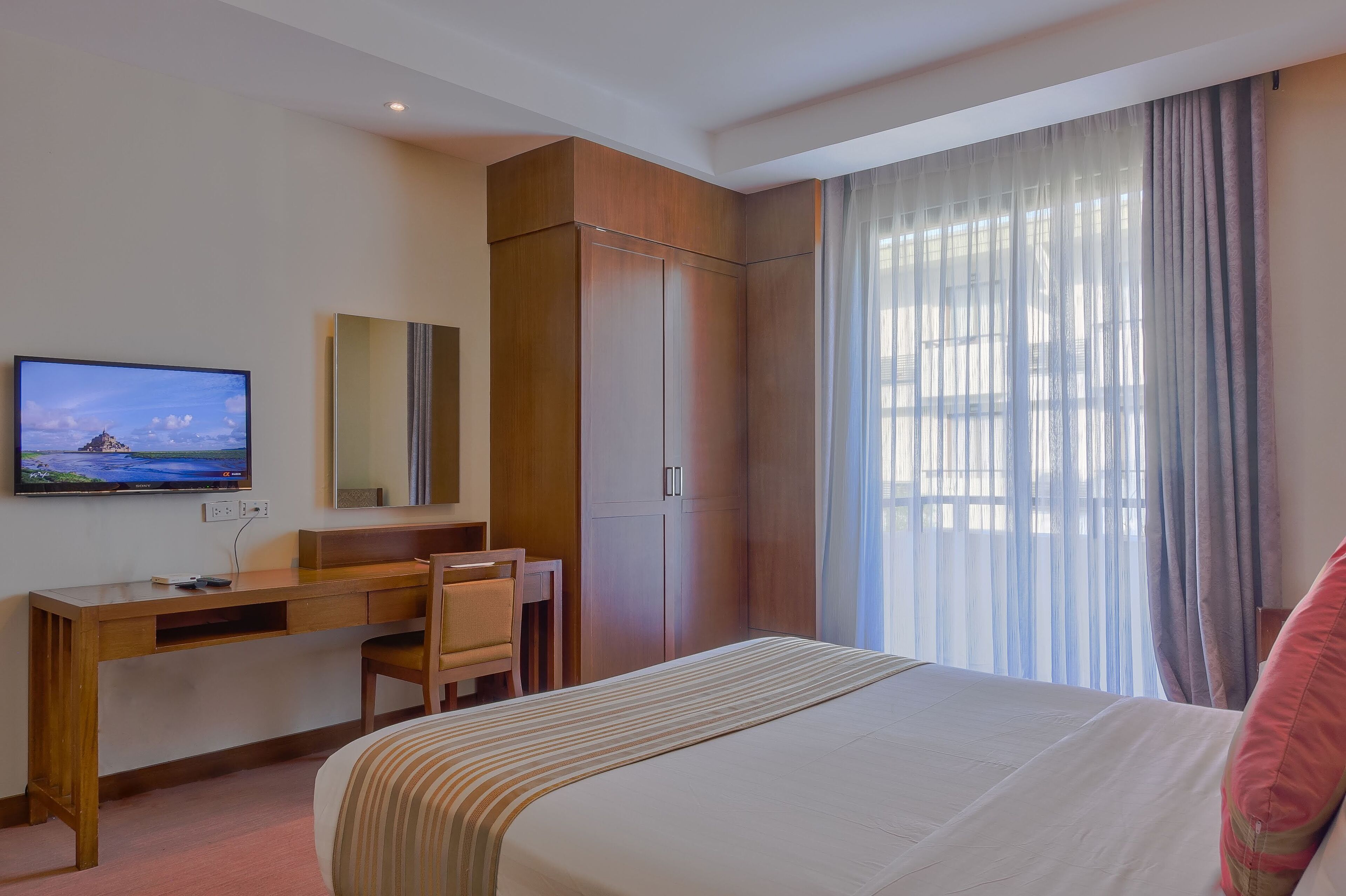 Ein Hotelzimmer mit einem Bett, einem Schreibtisch mit Stuhl, einem Fernseher und einem Kleiderschrank.