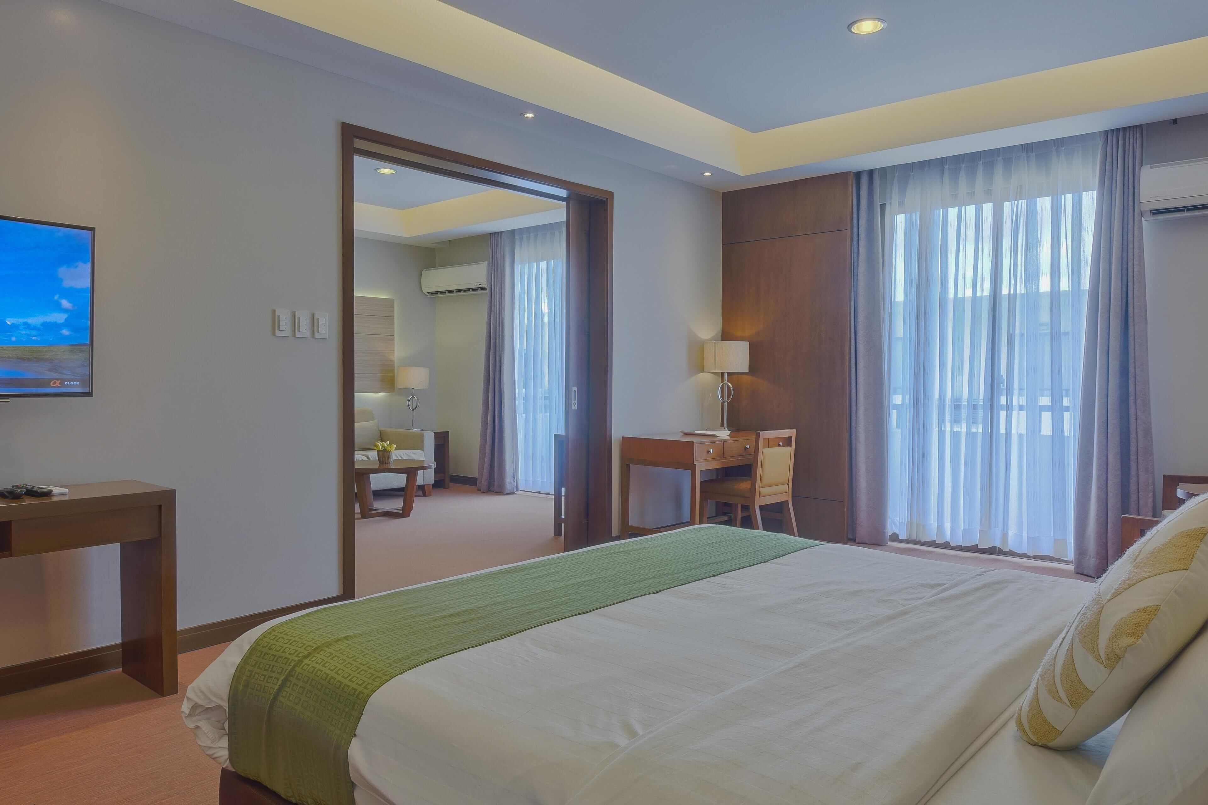 A hotel room with a large bed, a desk, a chair, a TV, and a bathroom visible through an open door.