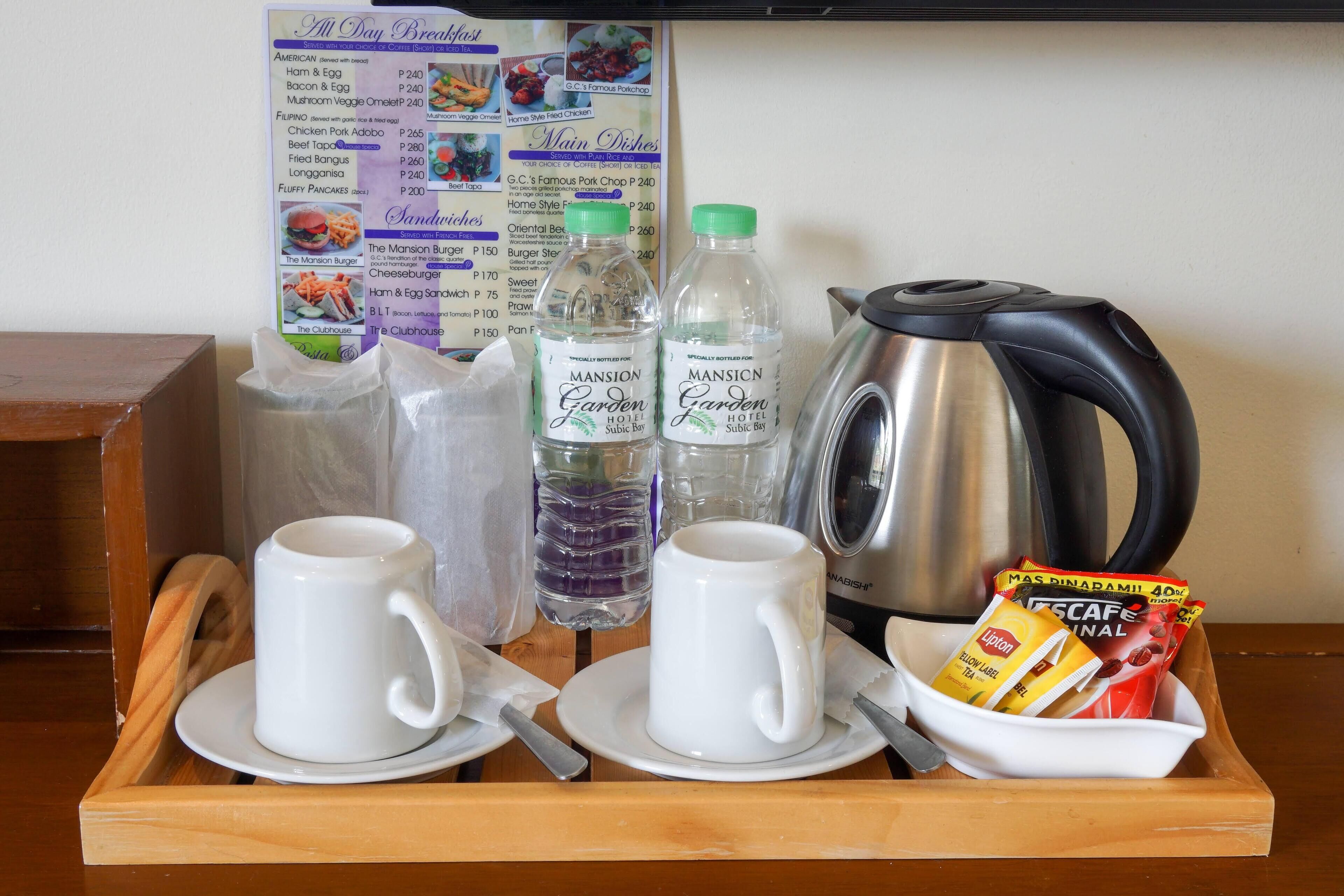 A breakfast tray with two white cups, two water bottles, a kettle, and a packet of instant coffee.