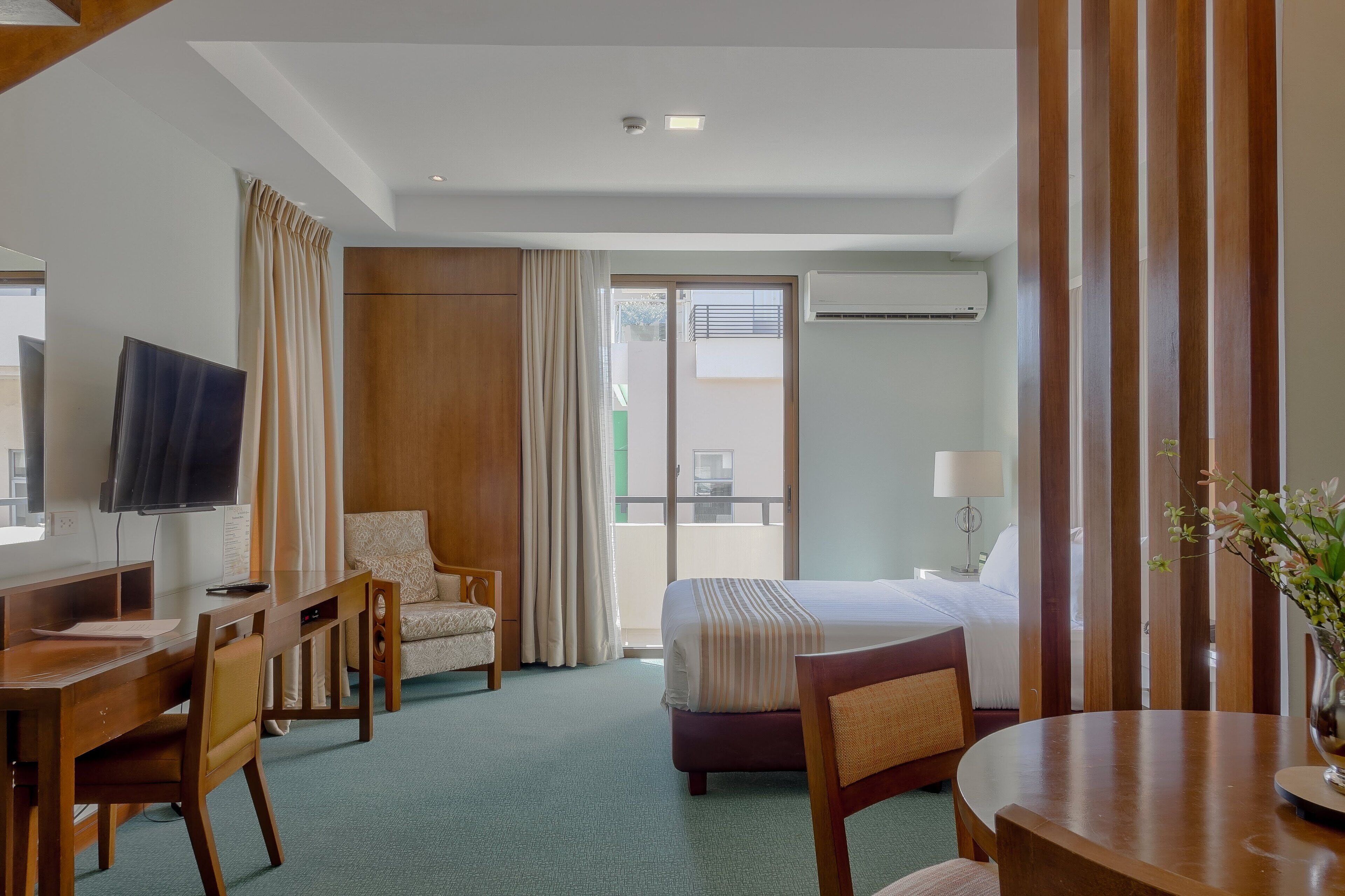 Habitación de hotel con cama, escritorio, silla, televisor, ventana con cortinas y equipo de aire acondicionado.