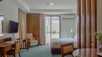 Habitación de hotel con cama, escritorio, silla, televisor, ventana con cortinas y equipo de aire acondicionado.