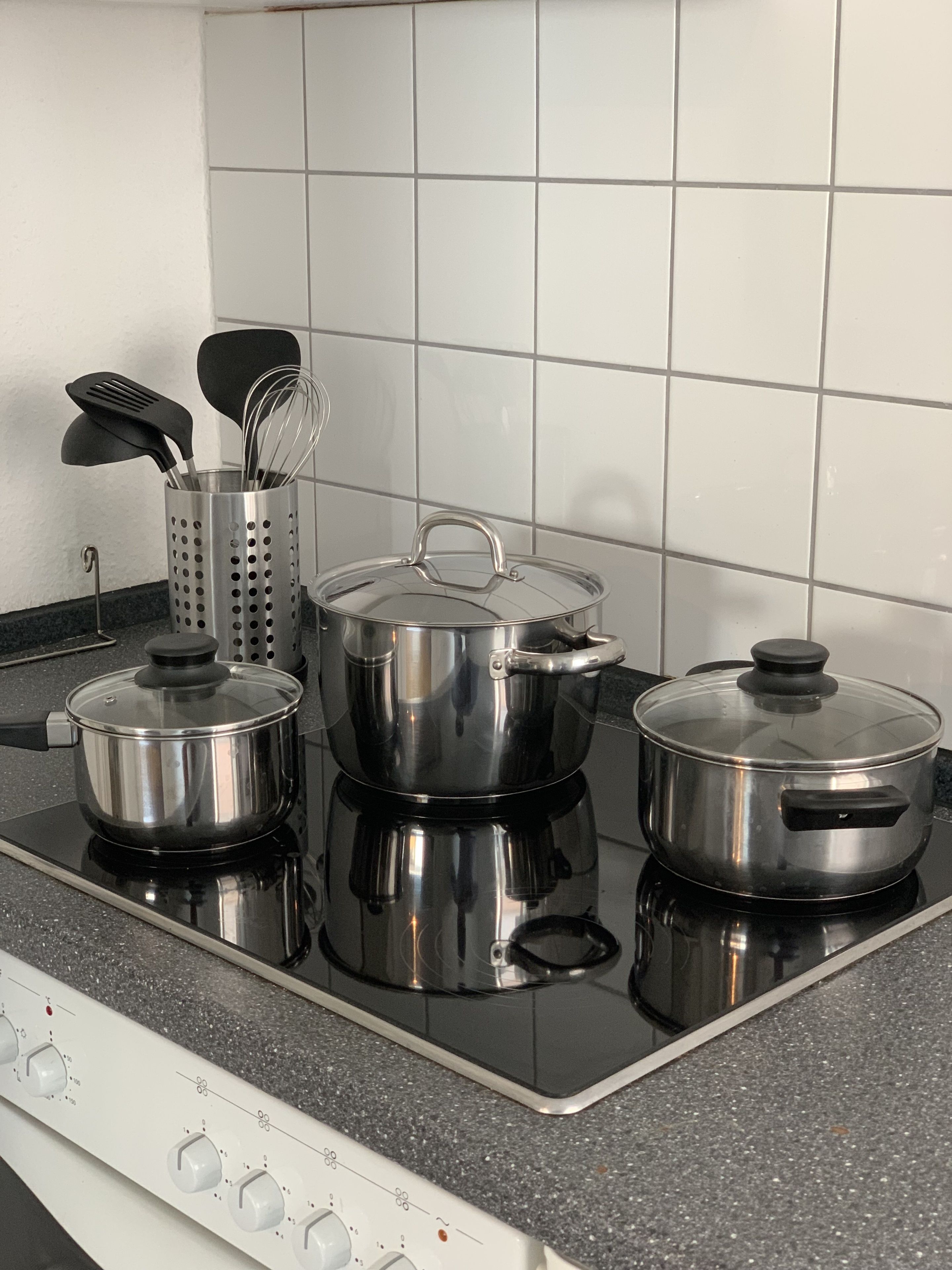 Uma cozinha com fogão, panelas e um porta-utensílios.