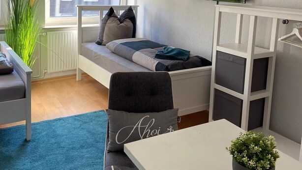 Ein kleines Schlafzimmer mit Bett, Schreibtisch, Stuhl, Fernseher und Fenster.