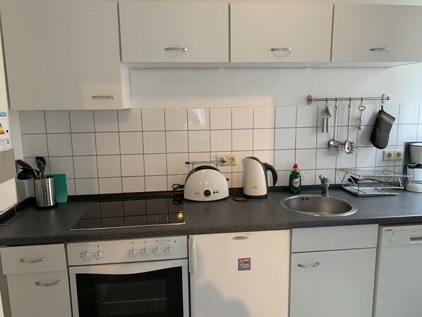 A kitchen with white cabinets, a black countertop, a kettle, a toaster, a dish rack, and a Siemens dishwasher. - City Studio Apartment (Bremerhaven)