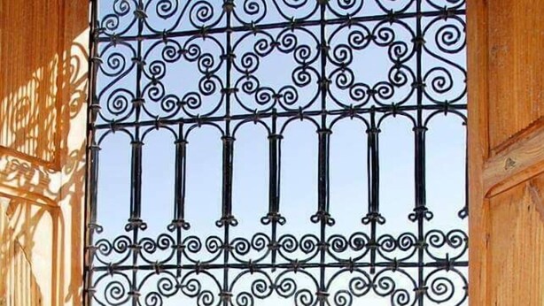 A wrought iron gate with a view of ancient ruins through it. - Kasbah Des Montagnes (Ighil N'Oumgoun)