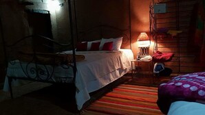 A dimly lit room with a bed, a bedside table with a lamp, and a striped carpet. - Kasbah Des Montagnes (Ighil N'Oumgoun)