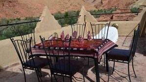 A terrace with a table set for two, surrounded by chairs, overlooking a mountainous landscape. - Kasbah Des Montagnes (Ighil N'Oumgoun)