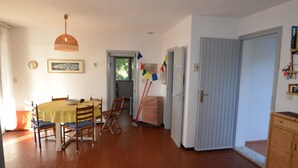 A dining area with a table, chairs, and a hanging light fixture. There is a door leading to another room and a window with blinds. - Ripa Dei Carrai (Capoliveri)