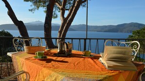 A table with a tablecloth, a book, a cup, and a kettle on a balcony overlooking a body of water and mountains. - Ripa Dei Carrai (Capoliveri)