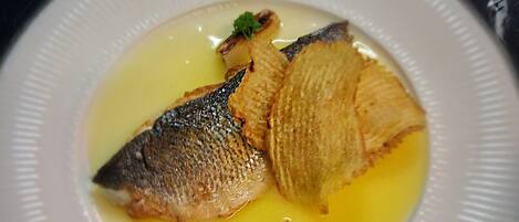 Un plato blanco con un pescado y una rebanada de pan sobre una superficie de mármol.