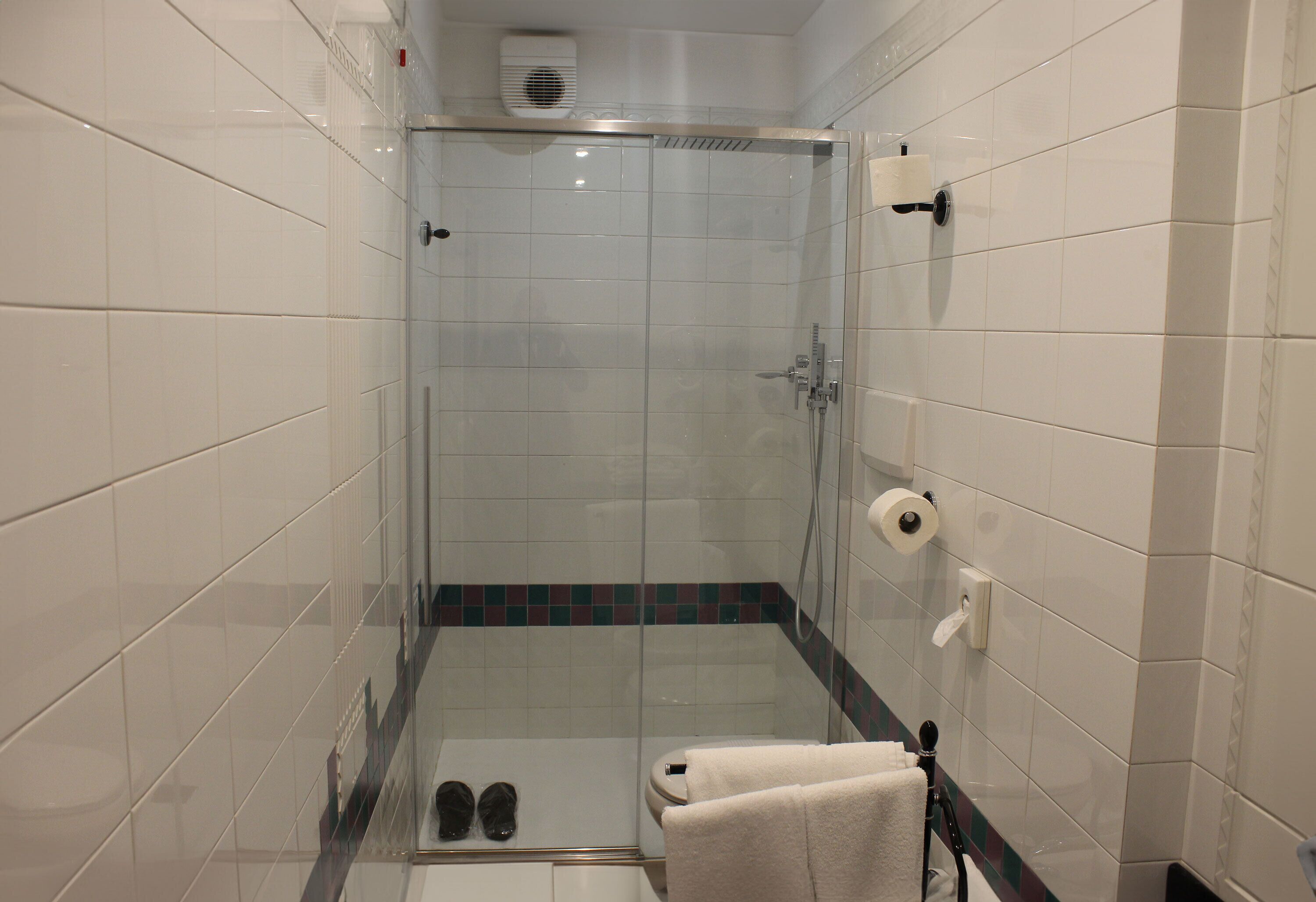 Un espacio de ducha pequeño y cerrado, con puerta de cristal, un perchero y un par de zapatos en el suelo.