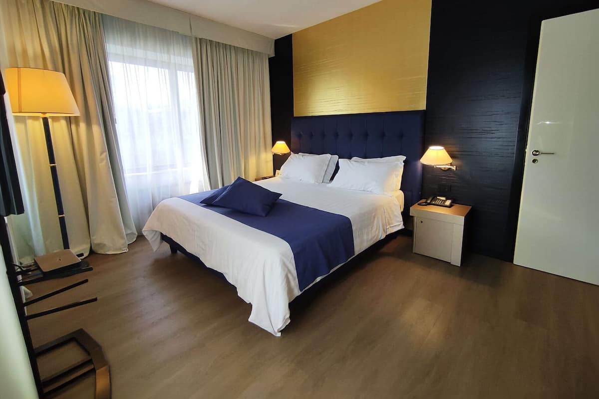 Una habitación de hotel con cama, lámparas de noche, escritorio y una silla.
