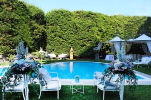 Un área junto a la piscina con sillones blancos, una carpa y arreglos florales.