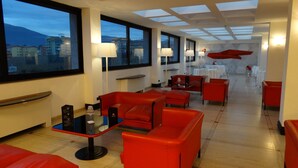 Un vestíbulo de hotel moderno con asientos rojos, ventanas amplias y vistas de la ciudad.