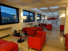 Un vestíbulo de hotel moderno con asientos rojos, ventanas amplias y vistas de la ciudad.