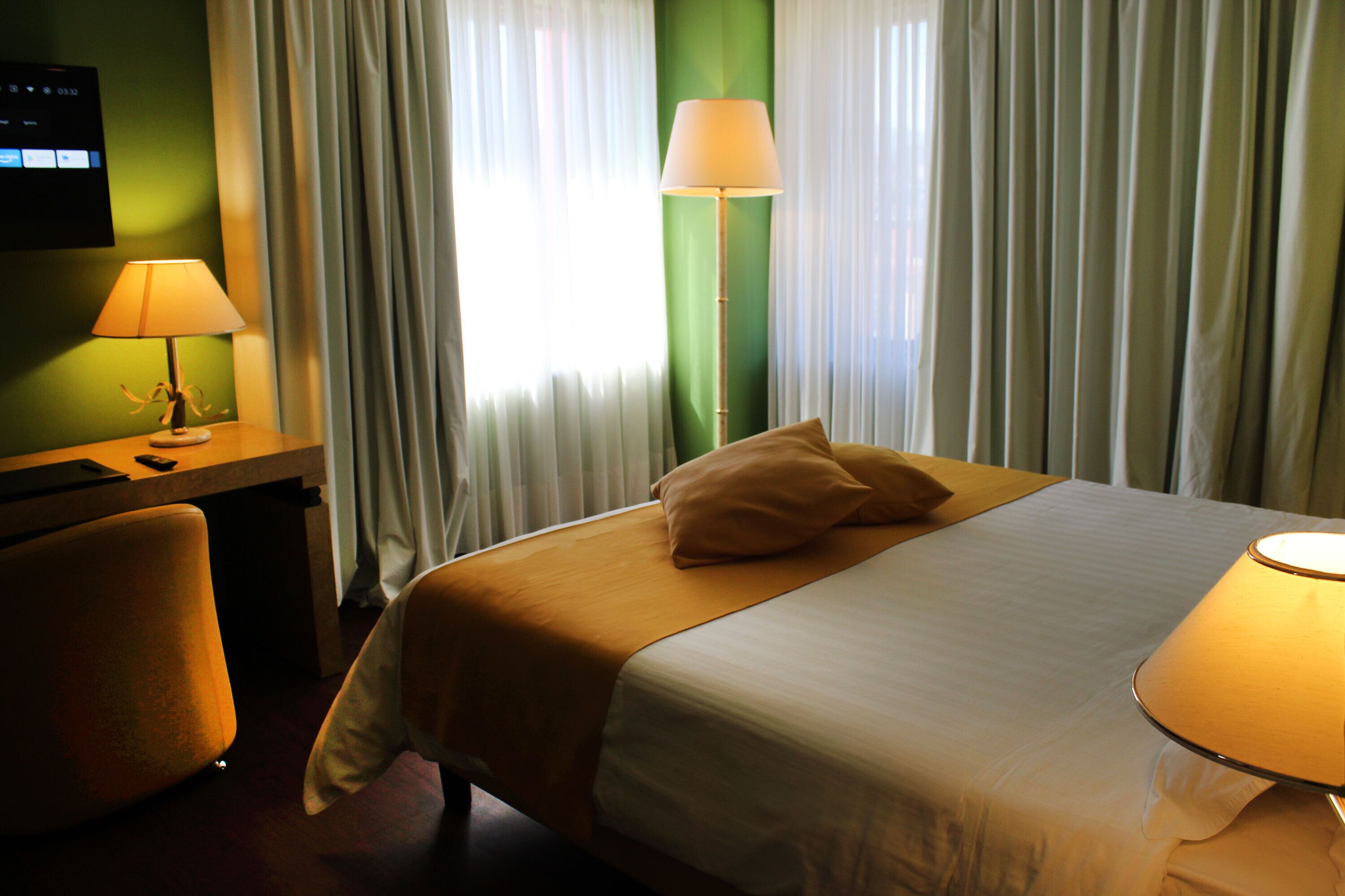Ein Hotelzimmer mit einem Bett, einem Schreibtisch und einem Stuhl. Eine Lampe steht auf dem Schreibtisch und eine weitere auf dem Nachttisch.