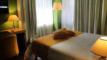 Ein Hotelzimmer mit einem Bett, einem Schreibtisch und einem Stuhl. Eine Lampe steht auf dem Schreibtisch und eine weitere auf dem Nachttisch.