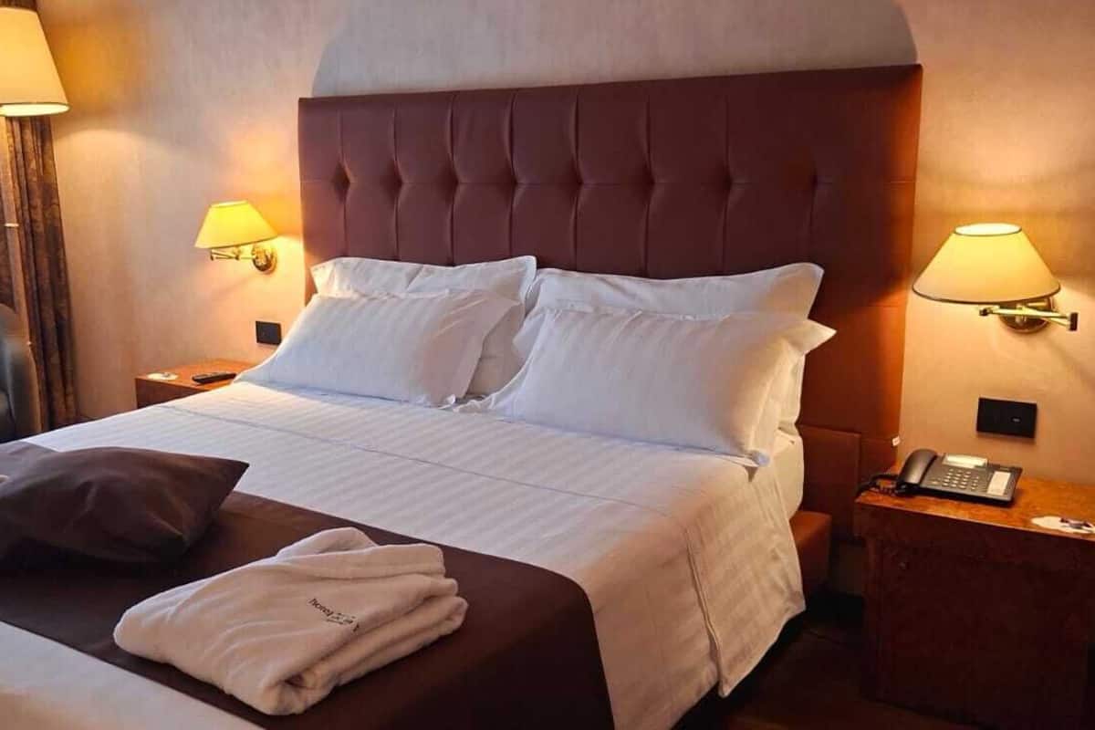 Una habitación de hotel con una cama grande, dos lámparas de noche, una silla, un escritorio con teléfono y una ventana con cortinas.
