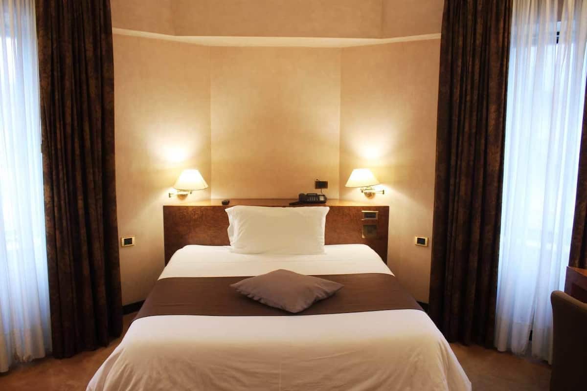Habitación de hotel con una cama grande, dos lámparas de noche y una mesita de noche con un teléfono.