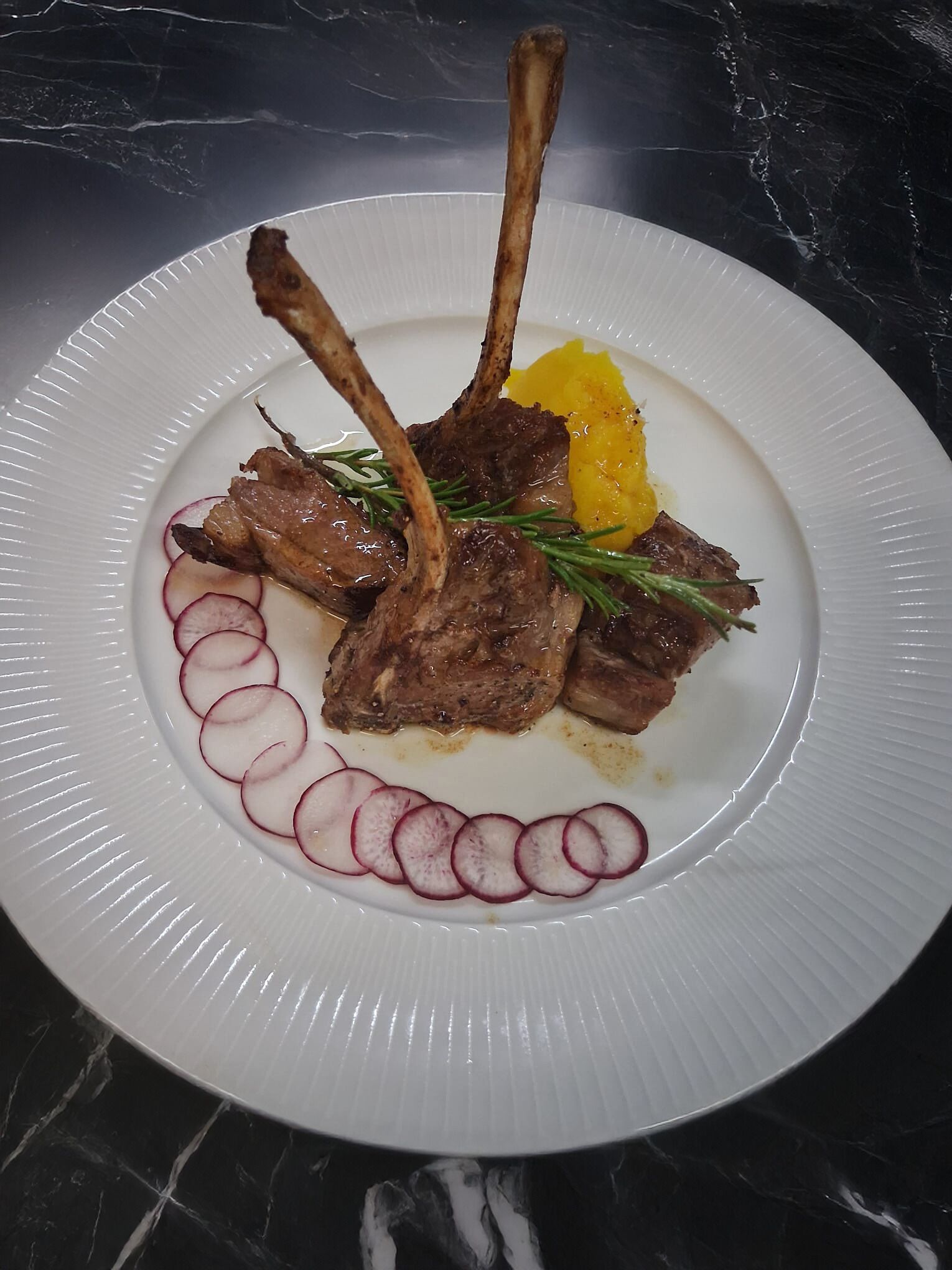 Un plato con chuletas de cordero, rebanadas de rábanos y una guarnición amarilla sobre un plato blanco.