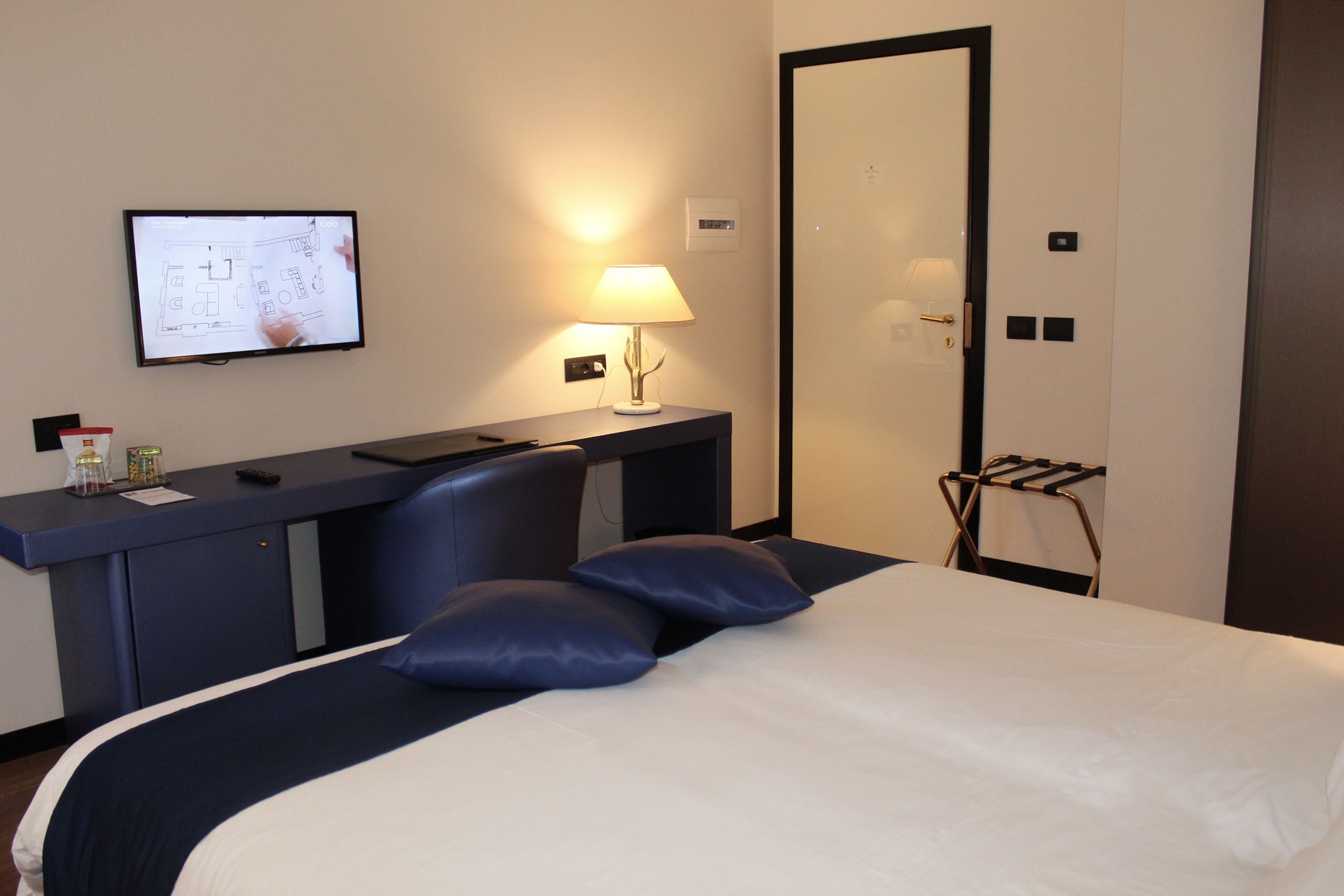 A hotel room with a bed, a desk, a chair, a TV, a lamp, and a wardrobe.