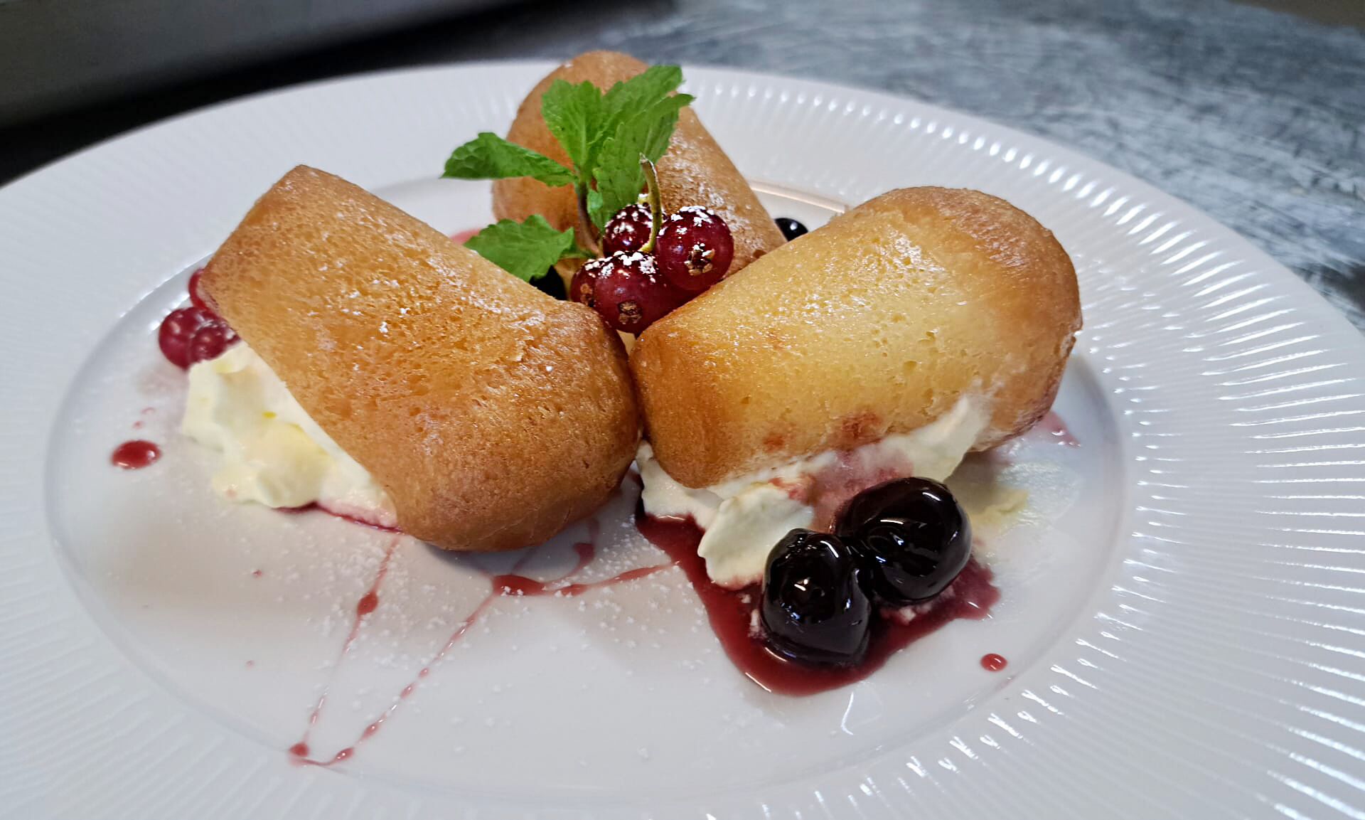 En desserttallerken med to kager, bær og et mynteblad.