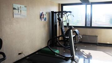 A gym with exercise equipment, a window with a view of buildings, and a poster on the wall.