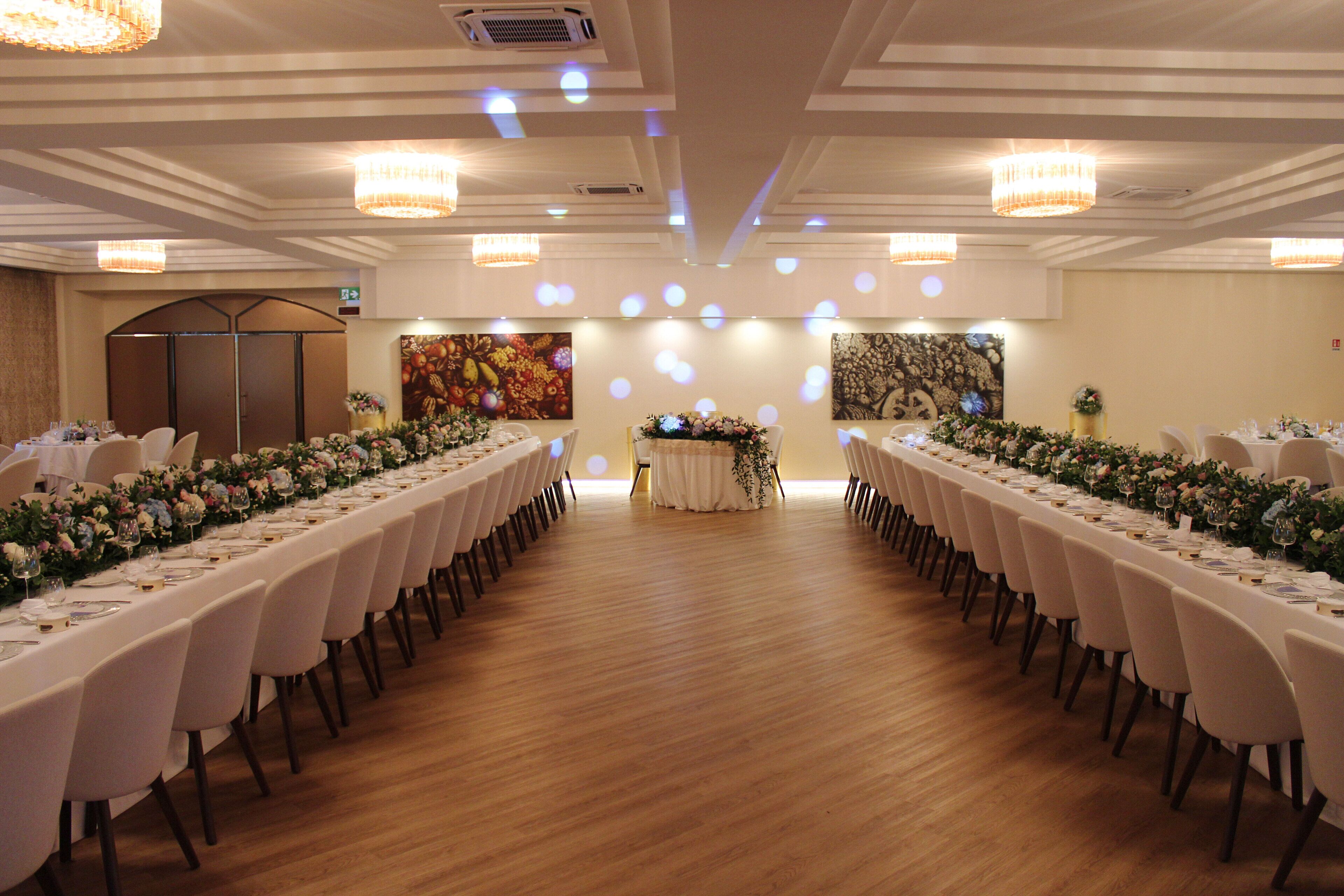 A banquet hall with long tables set for a formal event, featuring chandeliers and floral centerpieces.
