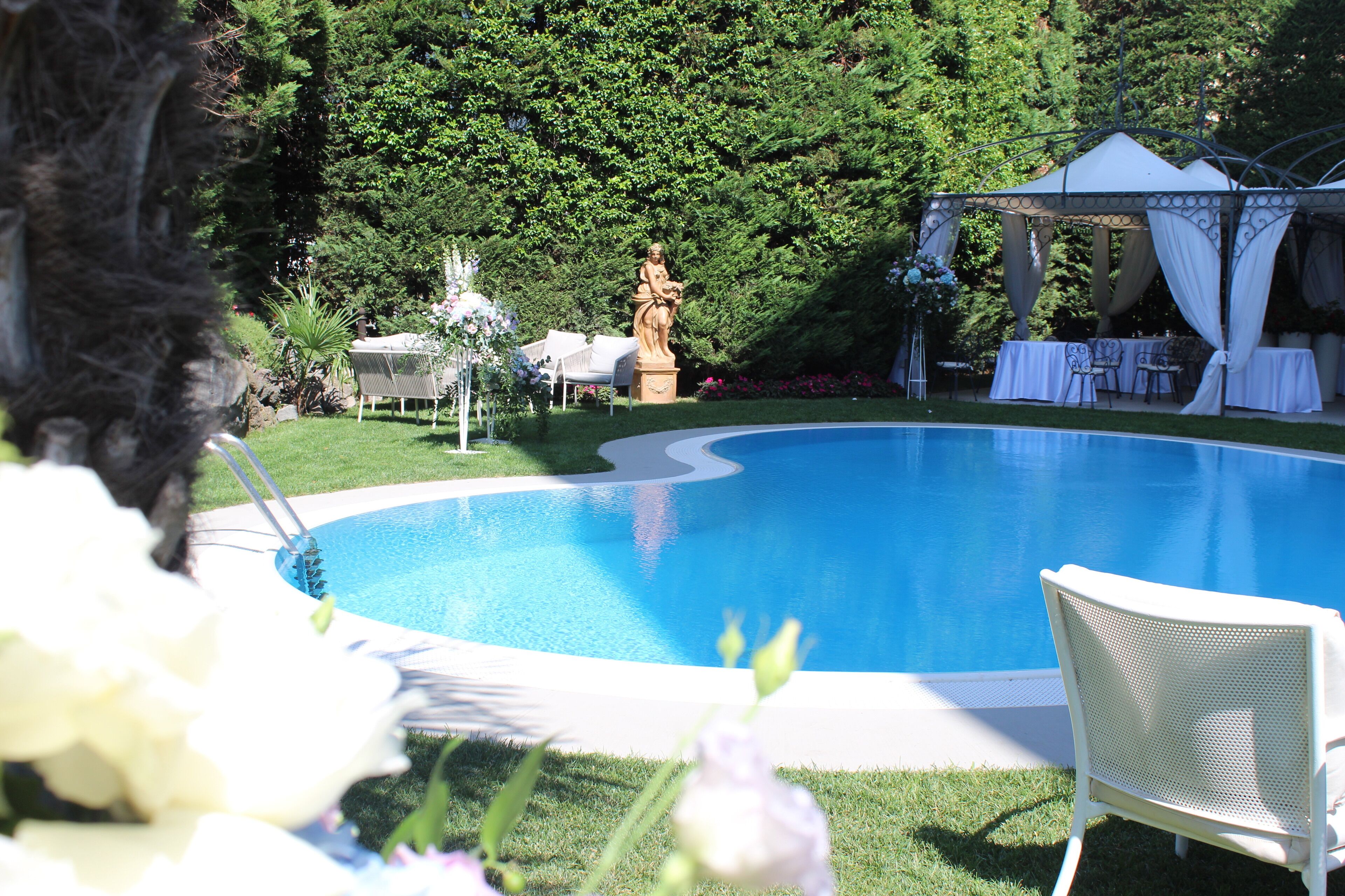Una piscina con una estatua, un pabellón y mobiliario exterior.