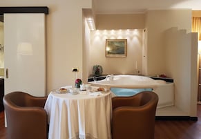 Una habitación con una mesa de comedor dispuesta para dos personas, una bañera y un cuadro en la pared.