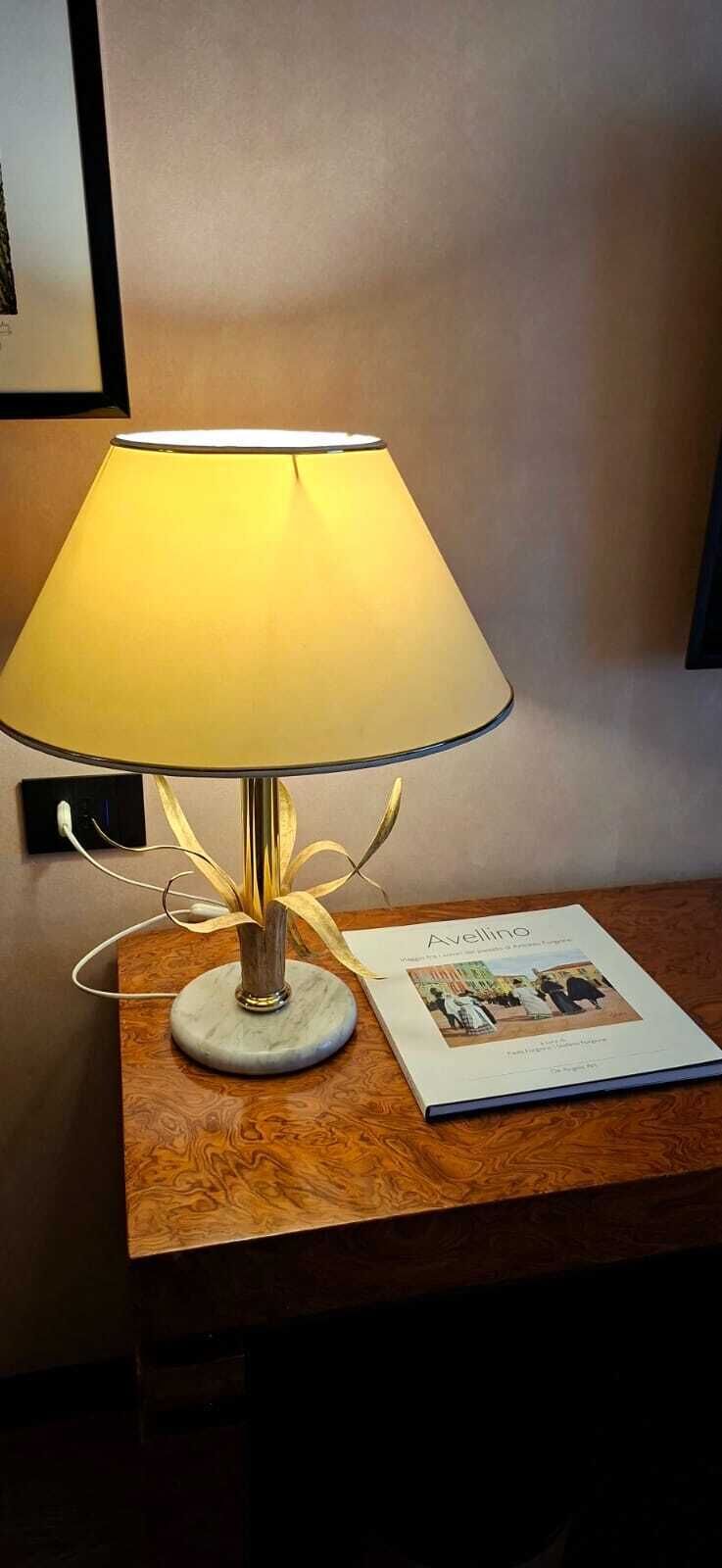 A lamp with a white shade and gold accents on a wooden table next to a book titled 'Avellino.'