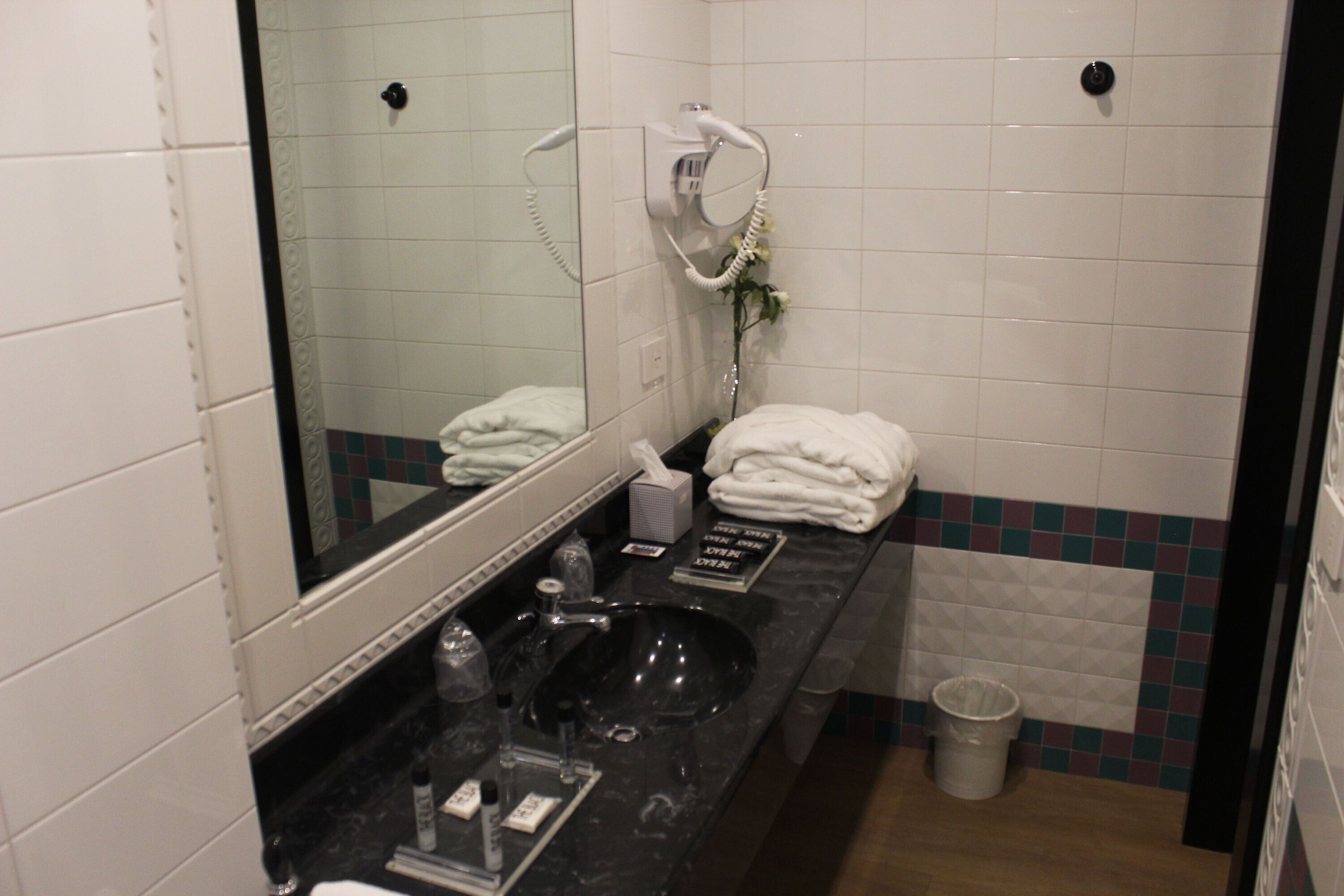 A bathroom with a black sink, a mirror, a towel rack, and a trash bin.